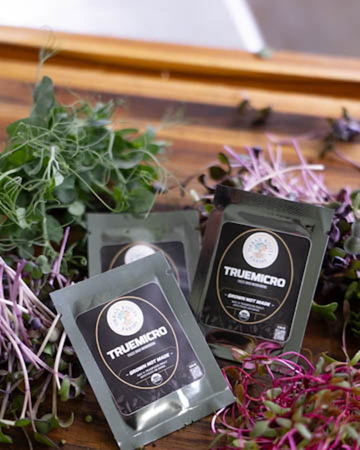TrueMicro single-serve travel packets on a wood bench with fresh microgreens