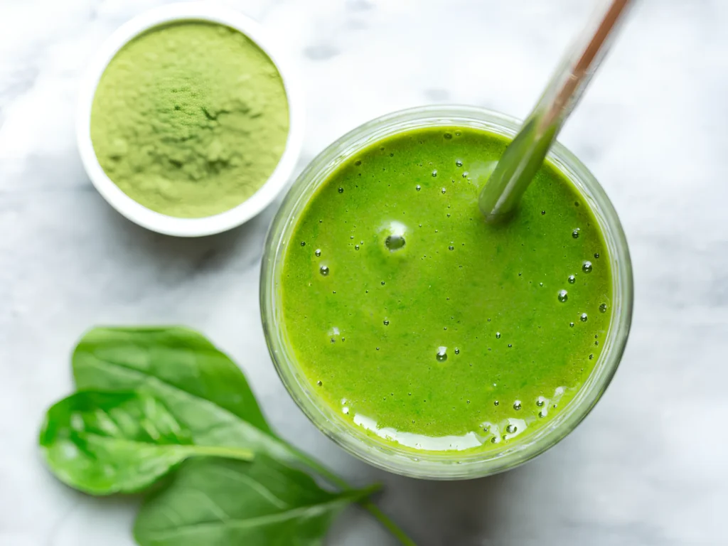 Image of a person adding green superfood powder to a smoothie.